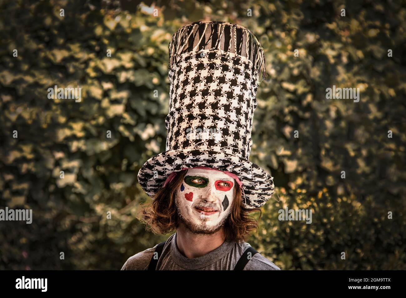 07-01-2019 Tulsa USA - Smiling young maan dressed like the Mad Hatter with painted face against bokeh leaves Stock Photo