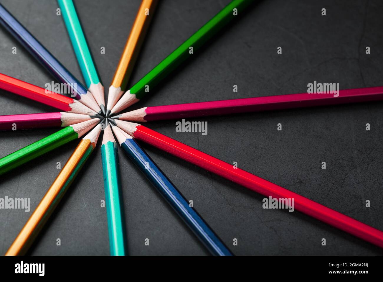 Wooden pencils of different colors in the shape of a star on a black background. Top view Stock Photo