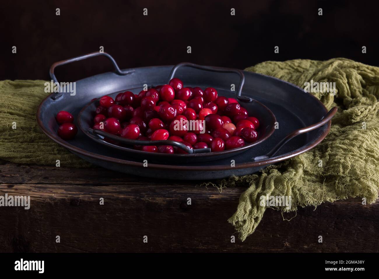 Still life with 2 rustic plates filled with fresh cranberries on an antique wooden table Stock Photo