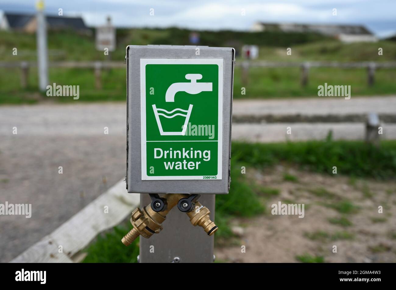 Drinking water sign with icon and two taps below. On metal post. Blurred background of road and grass. Stock Photo