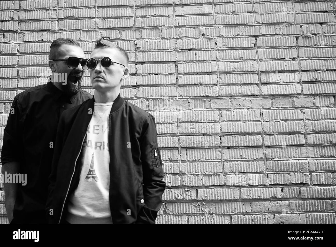 Two men in sunglasses against a brick wall background Stock Photo - Alamy