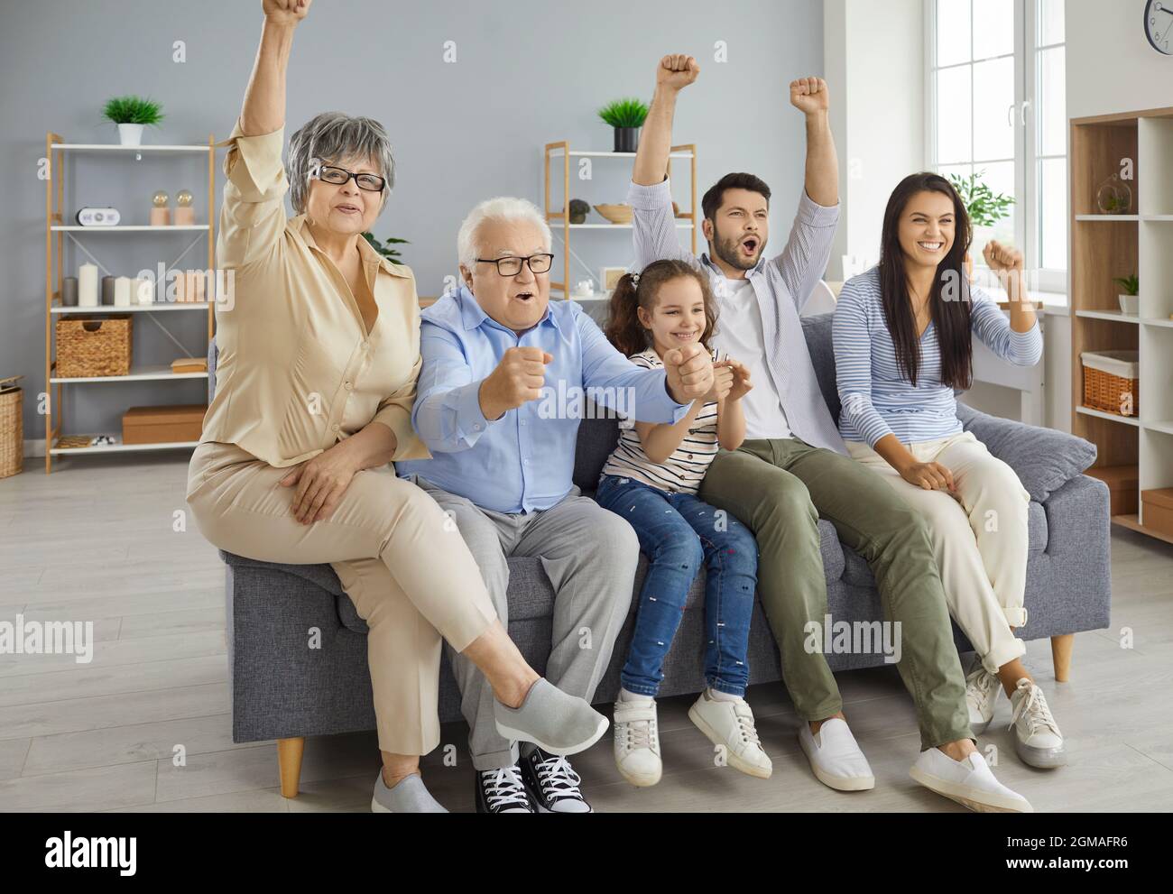 Multi-generational family sitting on couch at home and watching soccer match on TV Stock Photo