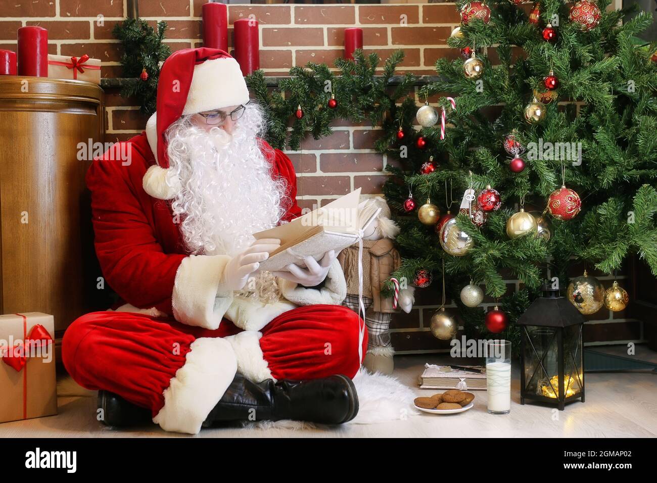 Santa Claus with gifts sitting next to a Christmas tree Stock Photo - Alamy