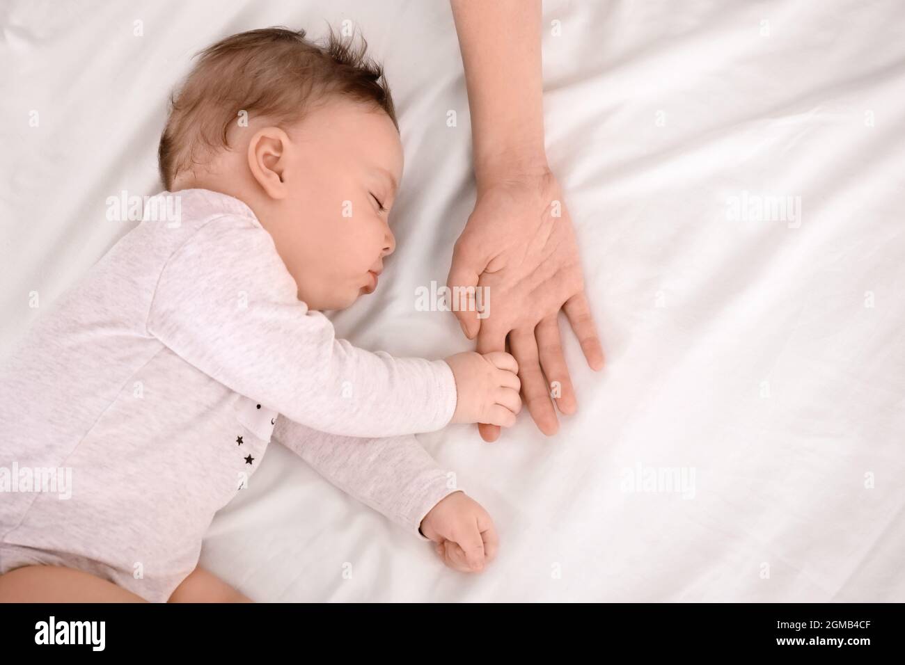 Sleeping baby holding mother s hand on bed Stock Photo Alamy