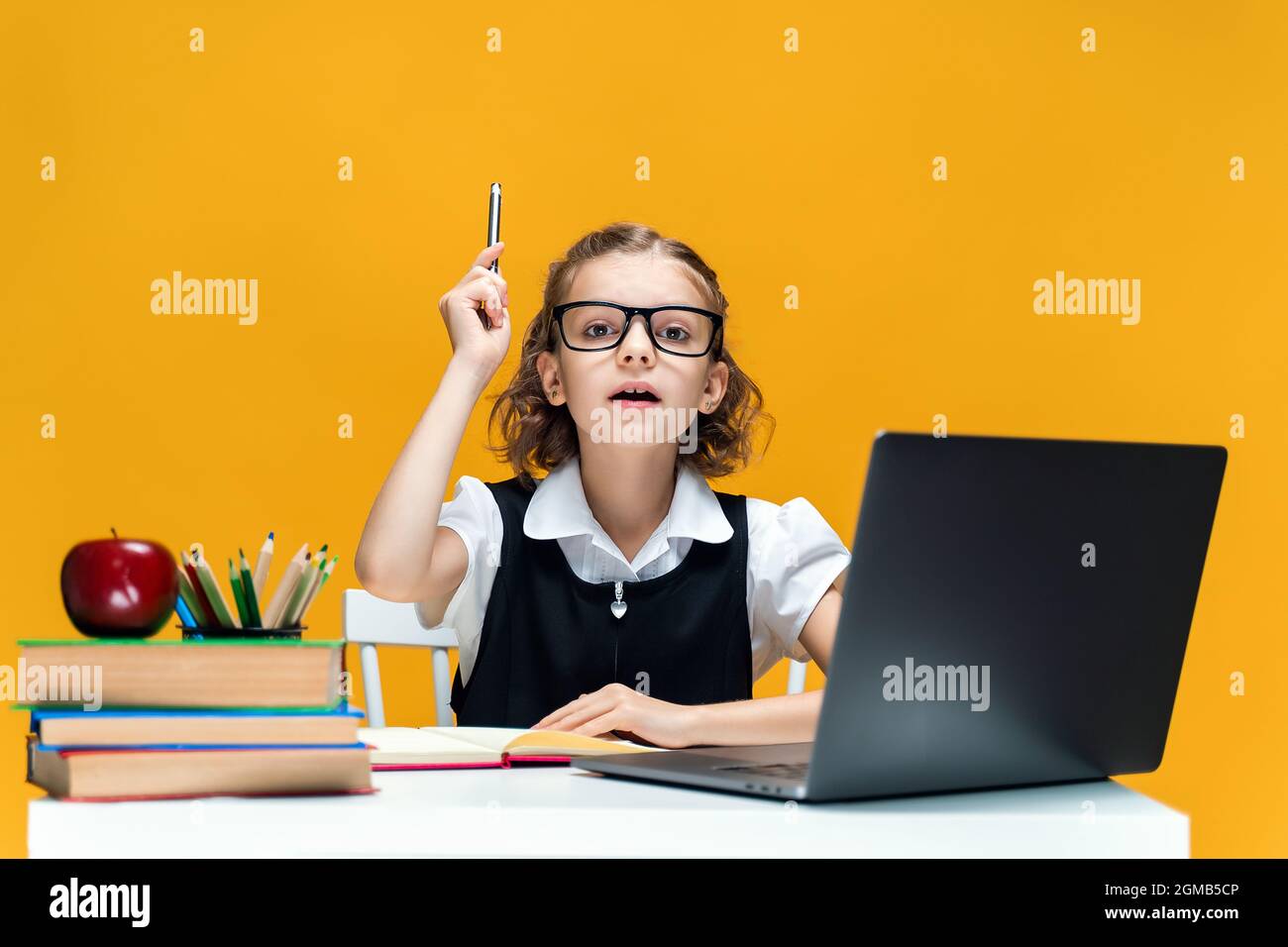 Serious schoolgirl in glasses raising pen up. Sitting at the desk with ...