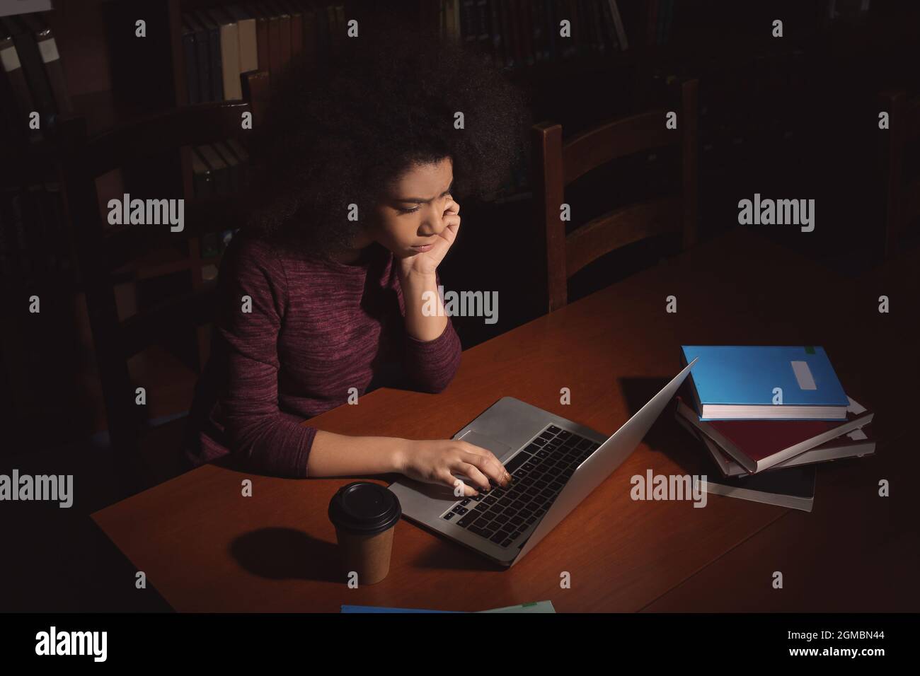African American student with laptop studying in library late at night ...