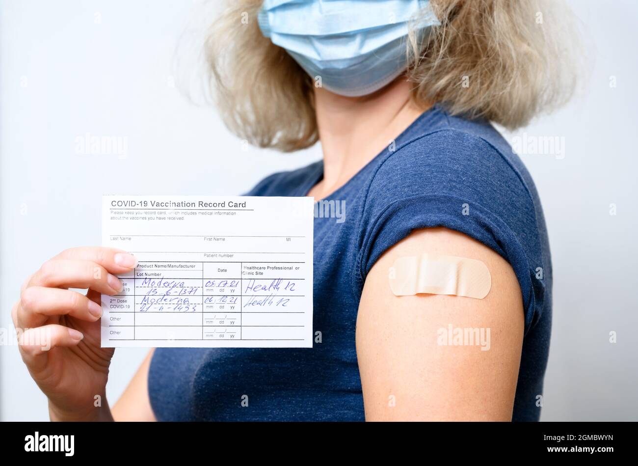 Vaccinated young woman in mask showing COVID-19 Vaccination Record Card, healthy person with plaster on arm after getting corona virus vaccine. Concep Stock Photo