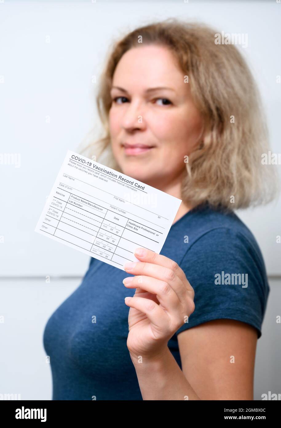 Vaccinated young woman showing COVID-19 Vaccination Record Card, happy person after getting corona virus vaccine. Concept of coronavirus vaccine shot, Stock Photo
