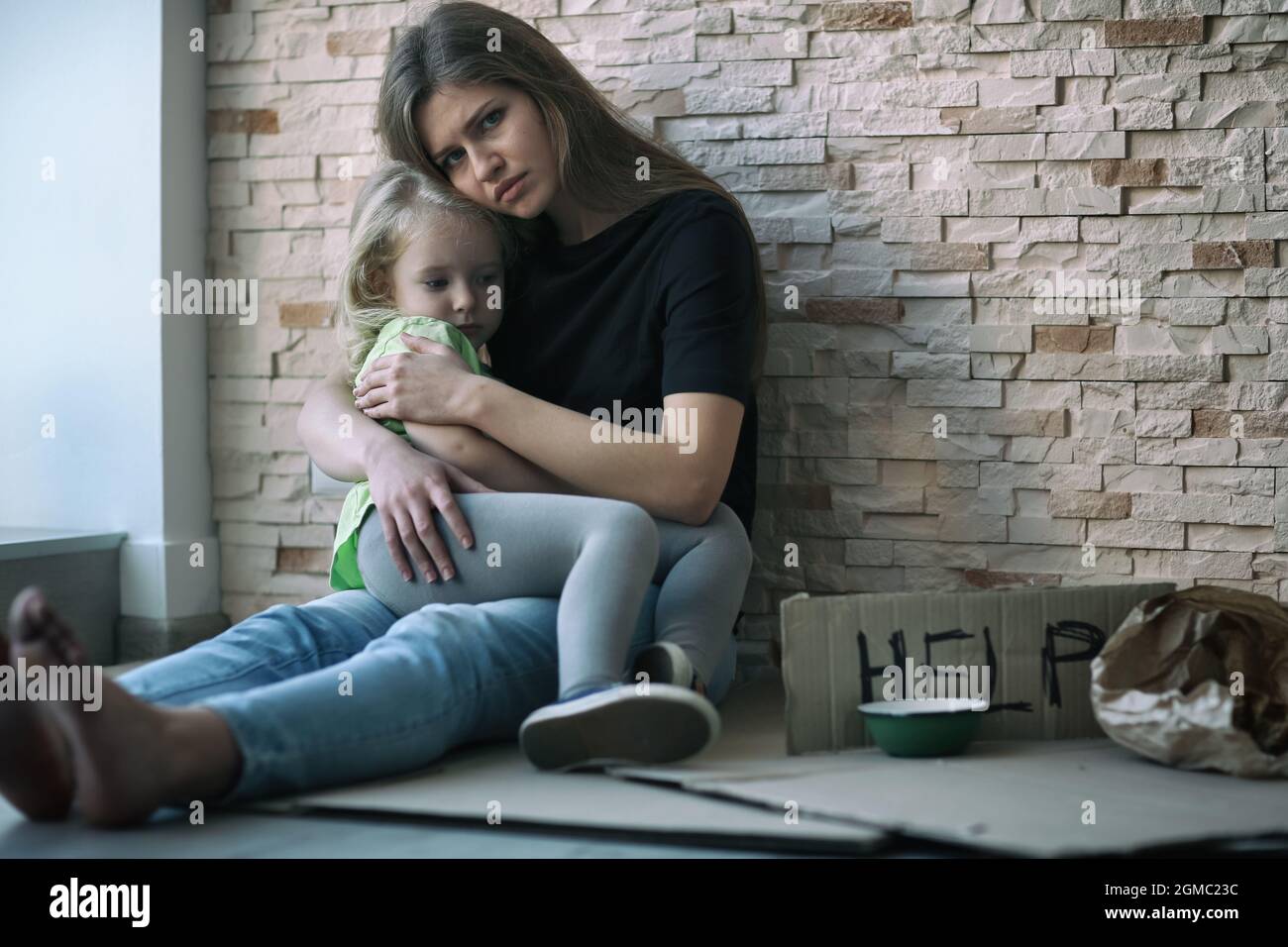 Homeless Poor Woman And Her Little Daughter Sitting Near Brick Wall And Asking For Help Stock