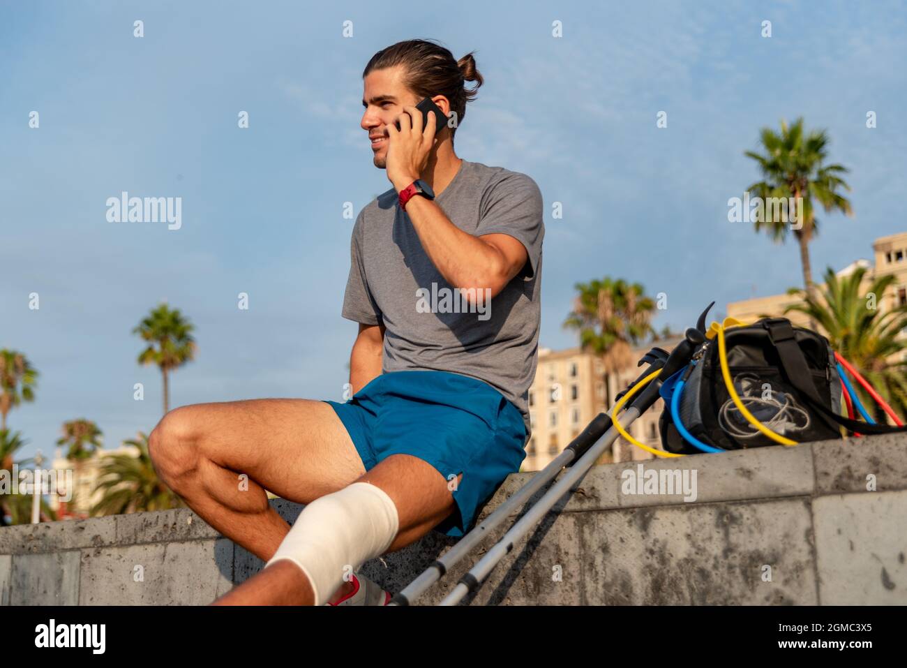 Young latin man with crutches using mobile phone after doing exercise Stock Photo