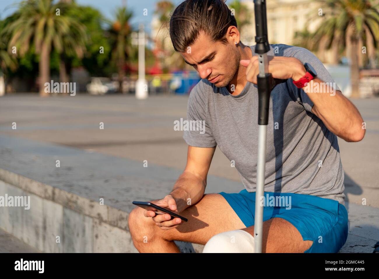 Young latin man with crutches using mobile phone after doing exercise Stock Photo