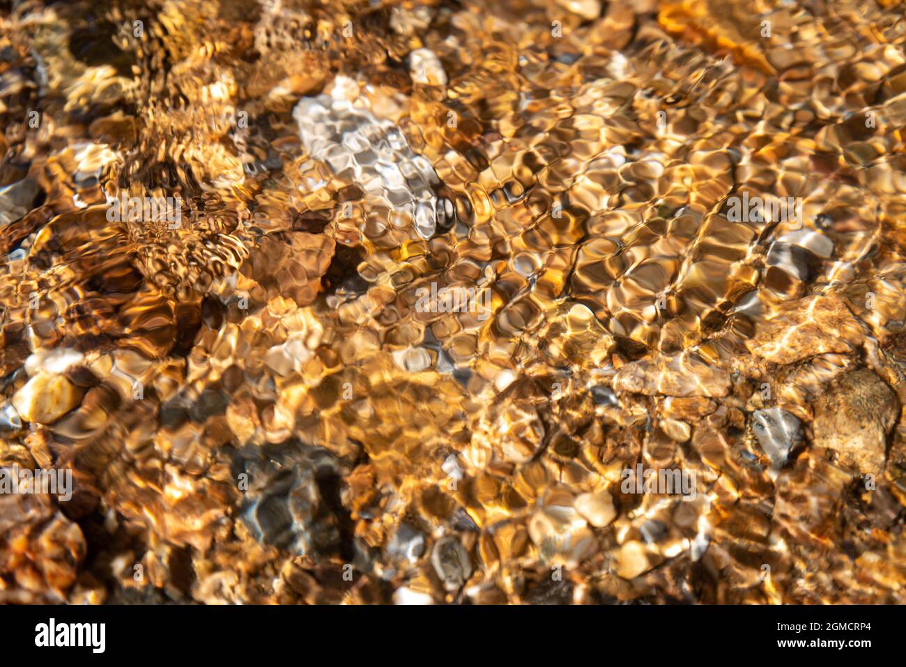 Abstract creek bed through clear flowing stream water with interference pattern Stock Photo