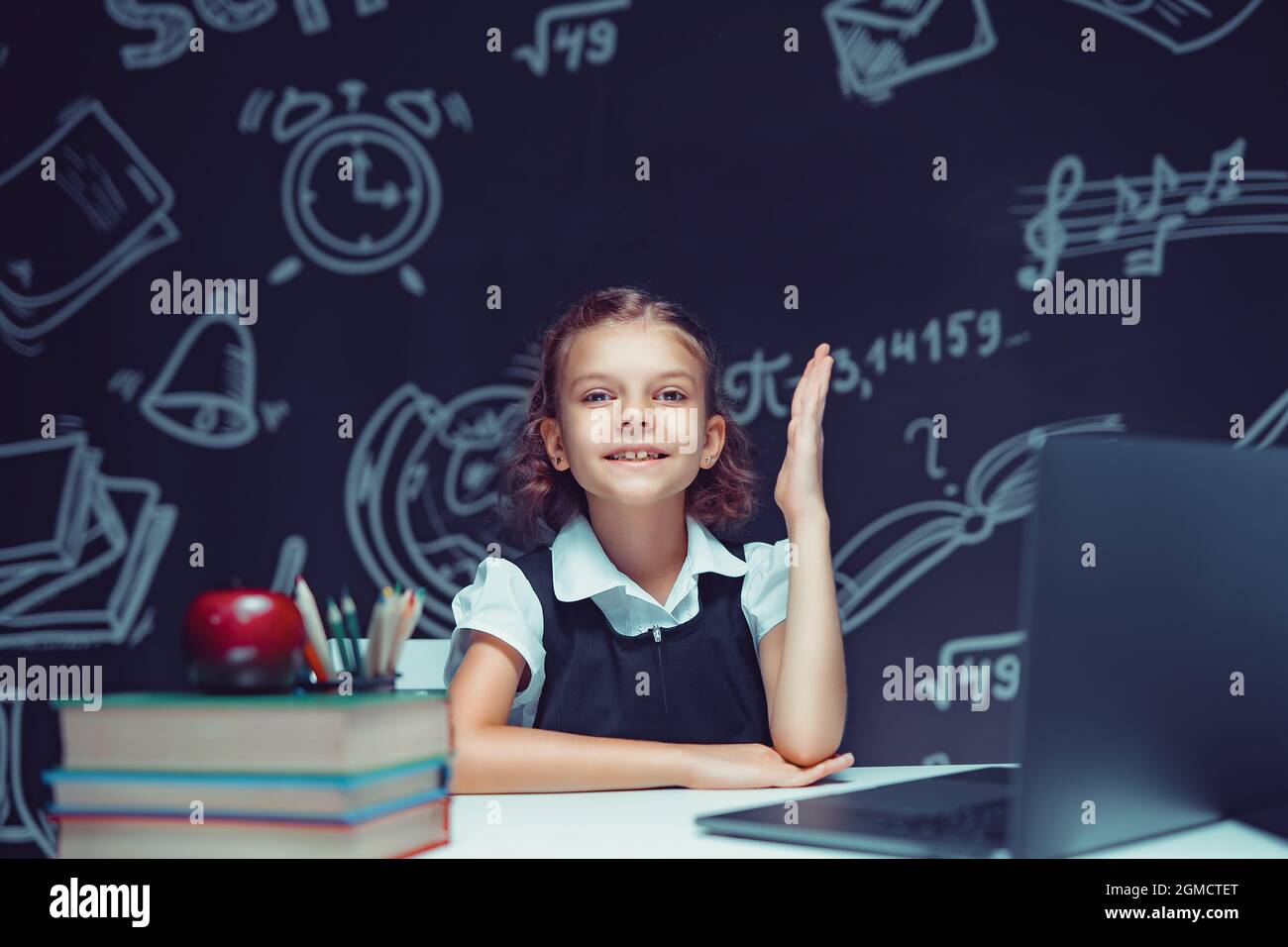 Happy schoolgirl raising hand sitting at laptop during online lesson ...
