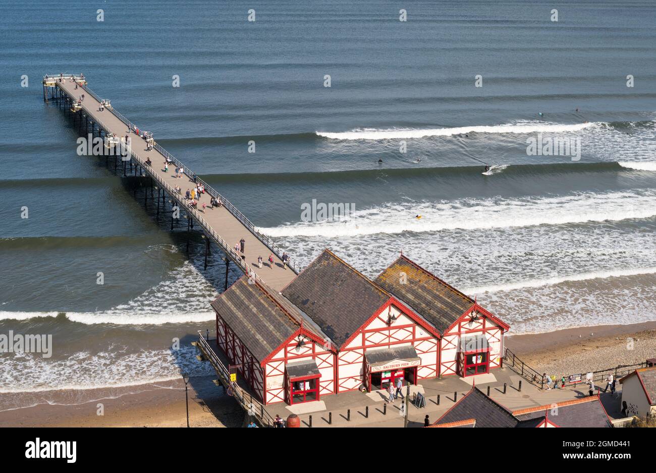 People walking along Saltburn pier with surfers in the water alongside, North Yorkshire, England, UK Stock Photo