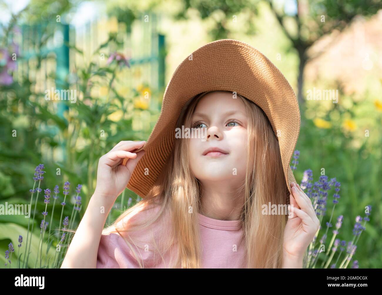 Little girl in a straw hat surrounded by lavender flowers. Portrait of ...