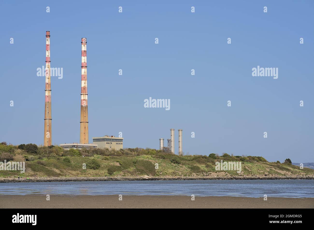 Closeup bright view of iconic Poolbeg power station chimneys and Poolbeg CCGT station against clear blue sky seen from Sandymount Beach, Dublin Stock Photo