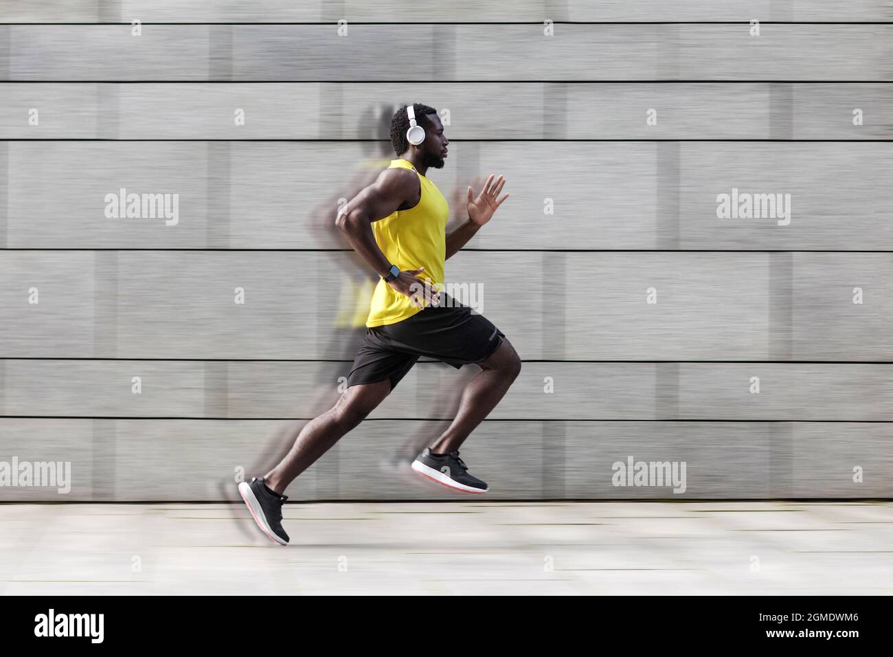 Profile side view of man runner with muscular body in tracksuit jogging against gray wall Stock Photo
