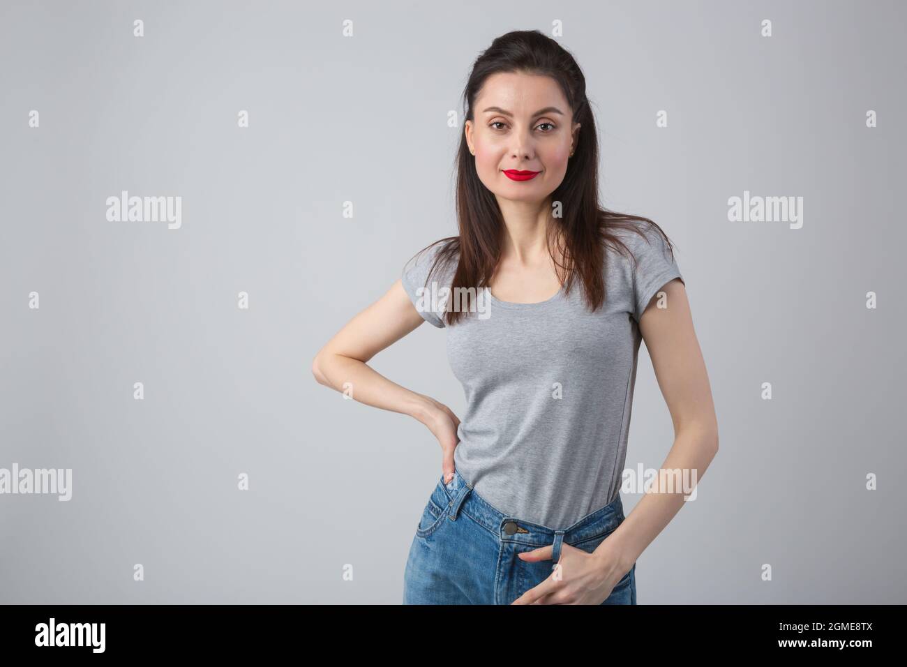 Portrait of pretty young brunette woman in mid 30s wearing casual clothes. Cute  female model in grey t-shirt and classic blue jeans on grey background  Stock Photo - Alamy