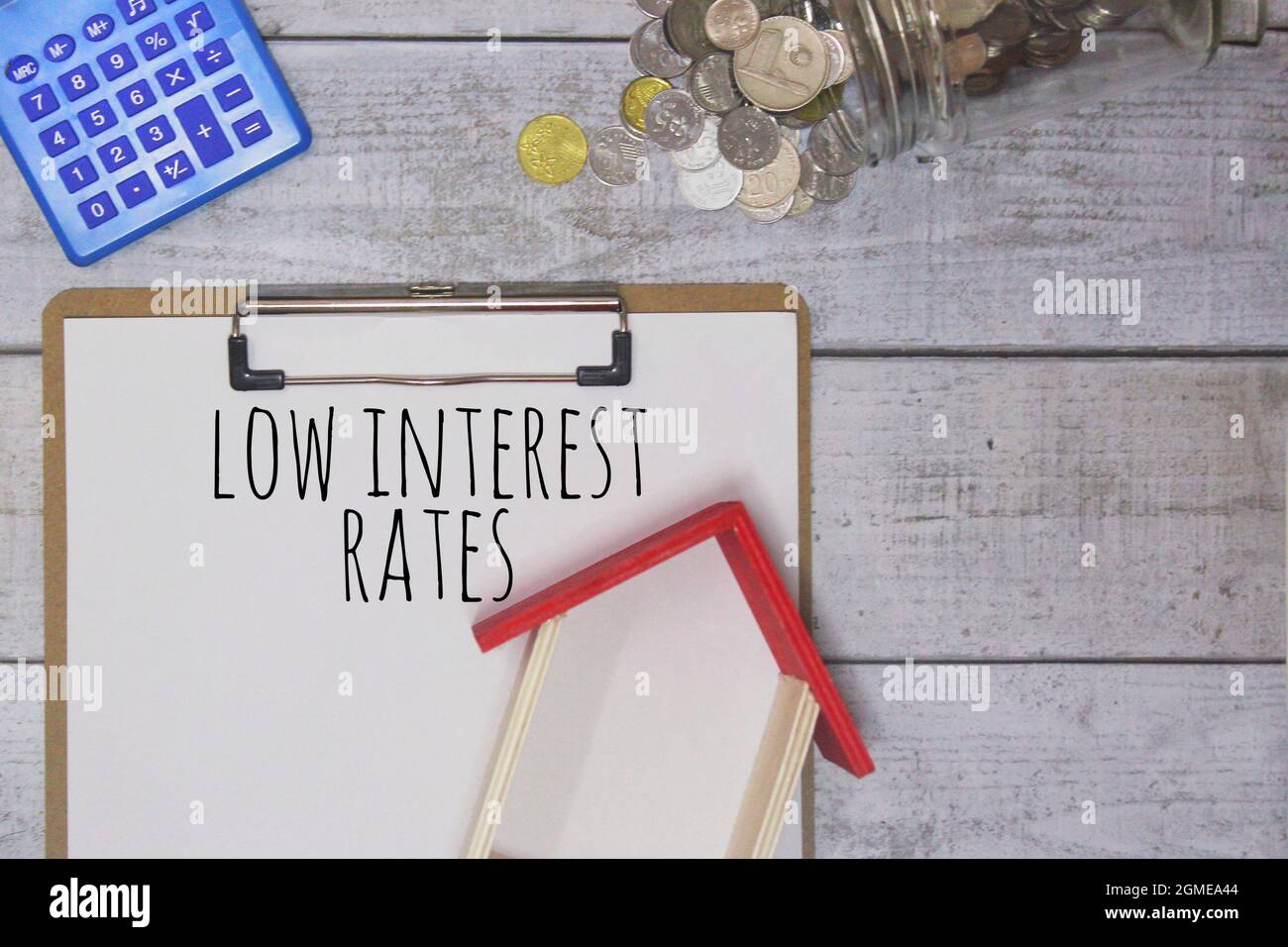 LOW INTEREST RATES text, miniature house, calculator and coins on wooden table. Stock Photo