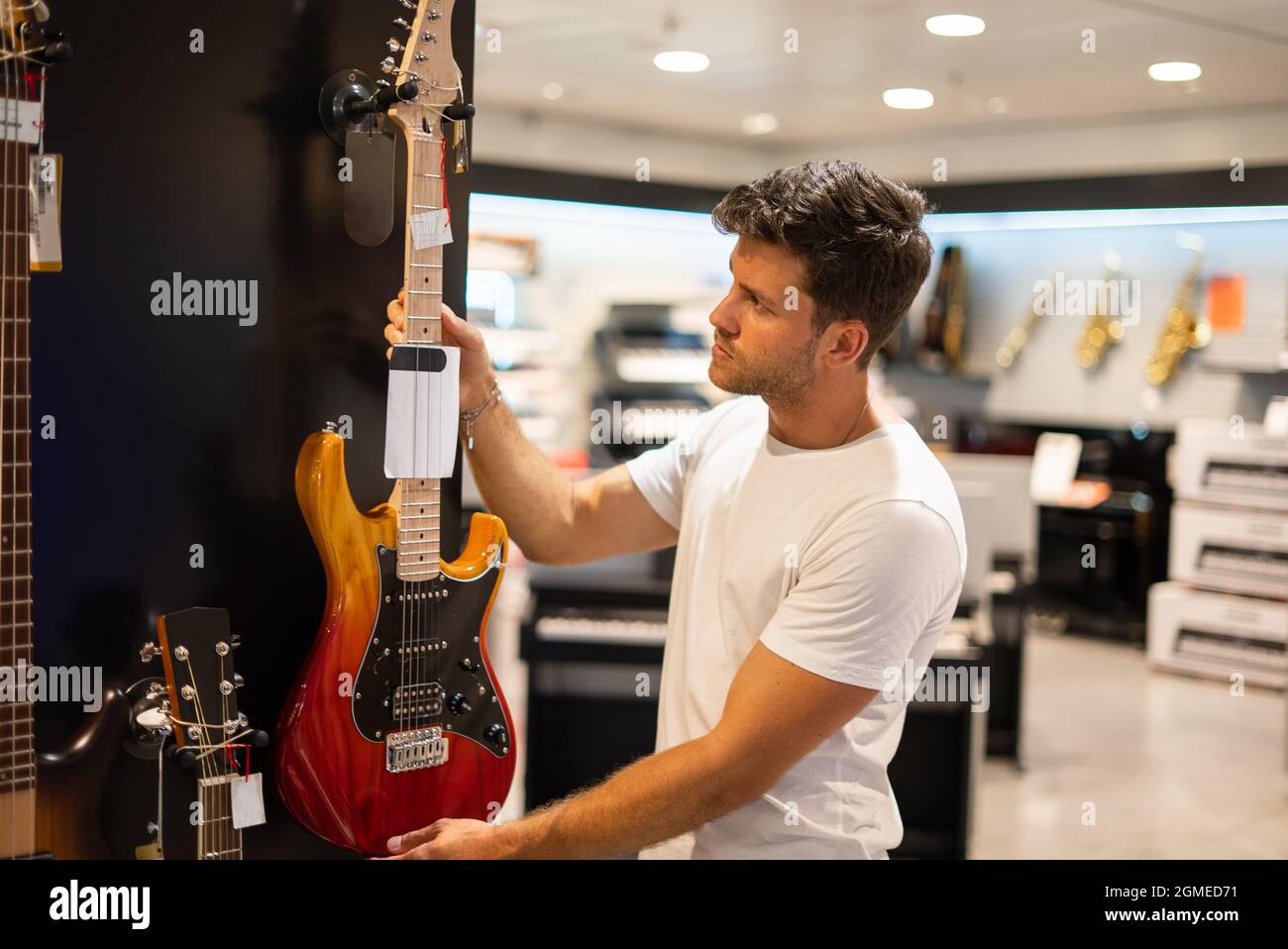 Side view of young male musician examining electric guitar hanging on ...