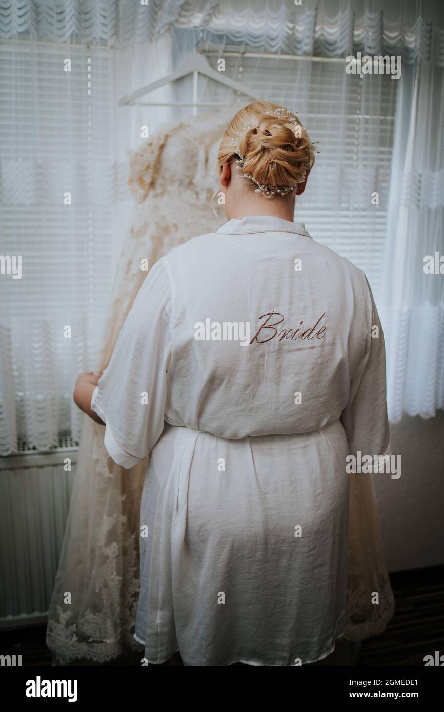 Bride wearing a dressing gown and looking at her wedding dress Stock