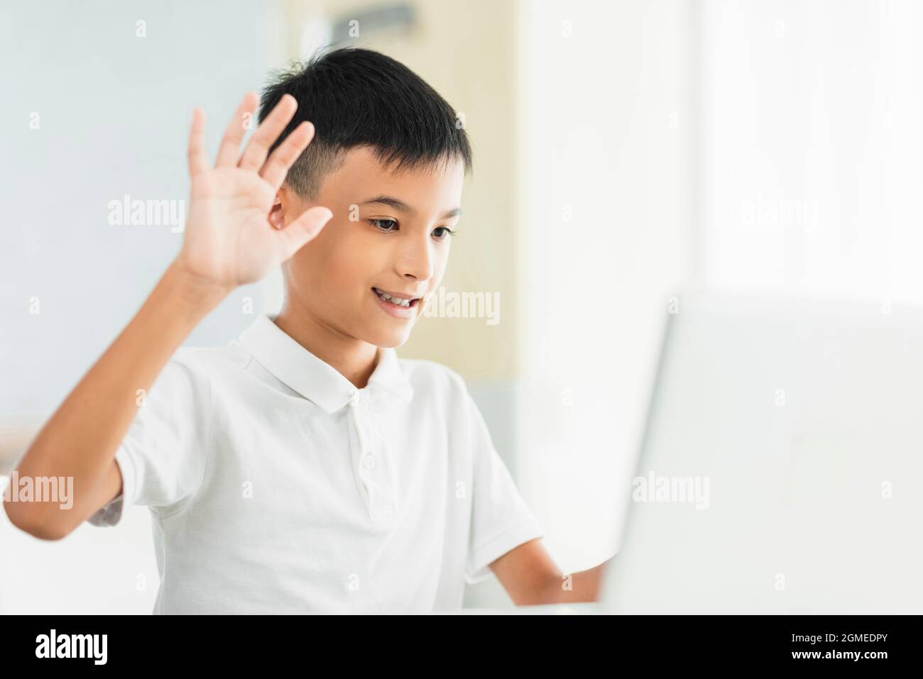 Boy using laptop to study and saying hi to teacher and classmate. Stock Photo