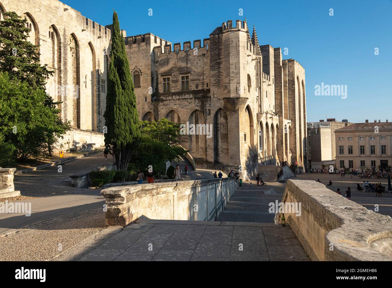 3 girls sit looking across Place du Palais towards the Palais des Papes, Avignon, France. Stock Photo