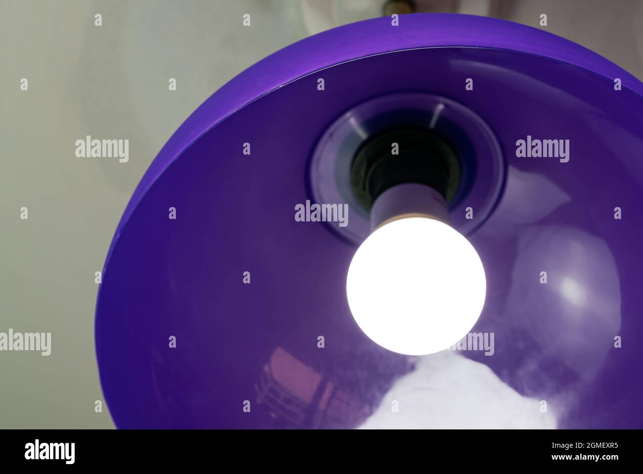 Lighting light bulb in purple plastic pendant at the ceiling in the room. Stock Photo
