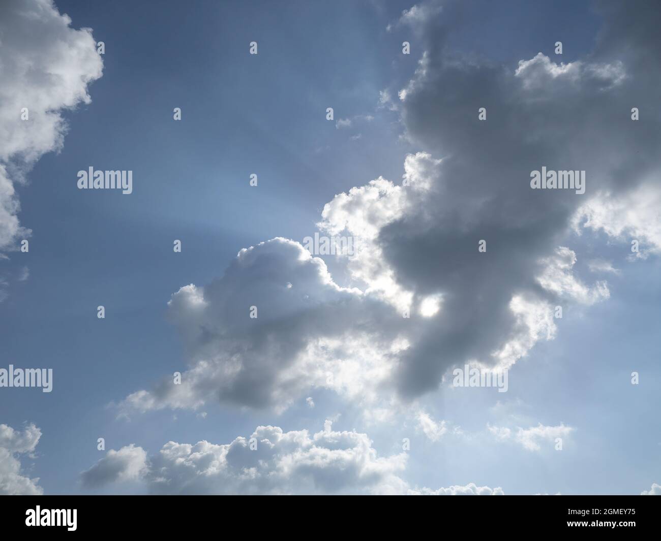 Sun overhead behind clouds in blue sky with light rays coming out from behind clouds Stock Photo