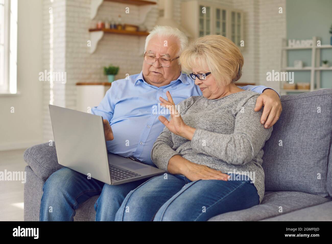 Aged senior couple waving hands greeting grandchildren through facetime using laptop. Stock Photo