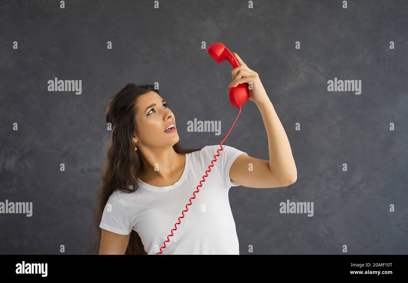 Surprised woman looks confused at red retro handset from landline phone she holds in her hand. Stock Photo