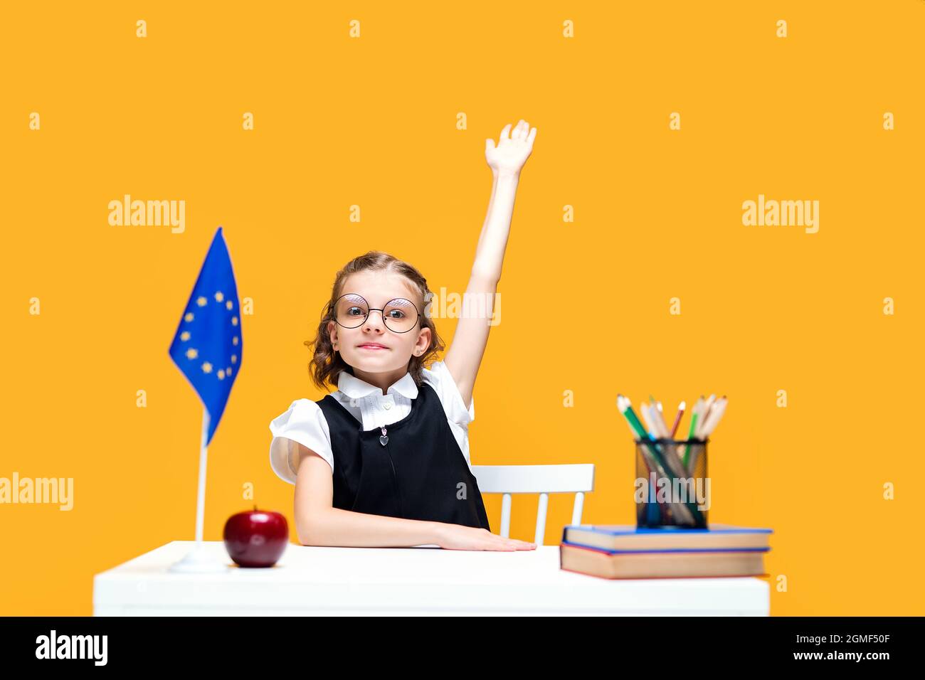 Caucasian schoolgirl raising hand up sitting at the desk during lesson ...