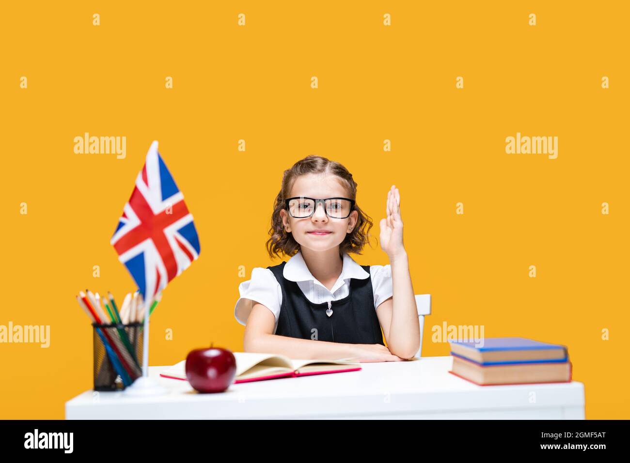 Smiling caucasian schoolgirl raising hand sitting at the desk. English ...