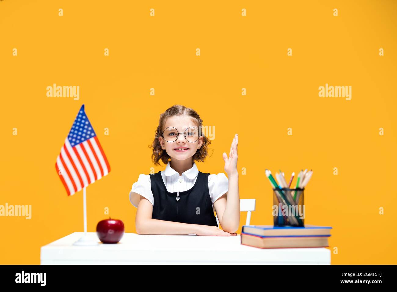 Smiling caucasian schoolgirl raising hand sitting at the desk during ...