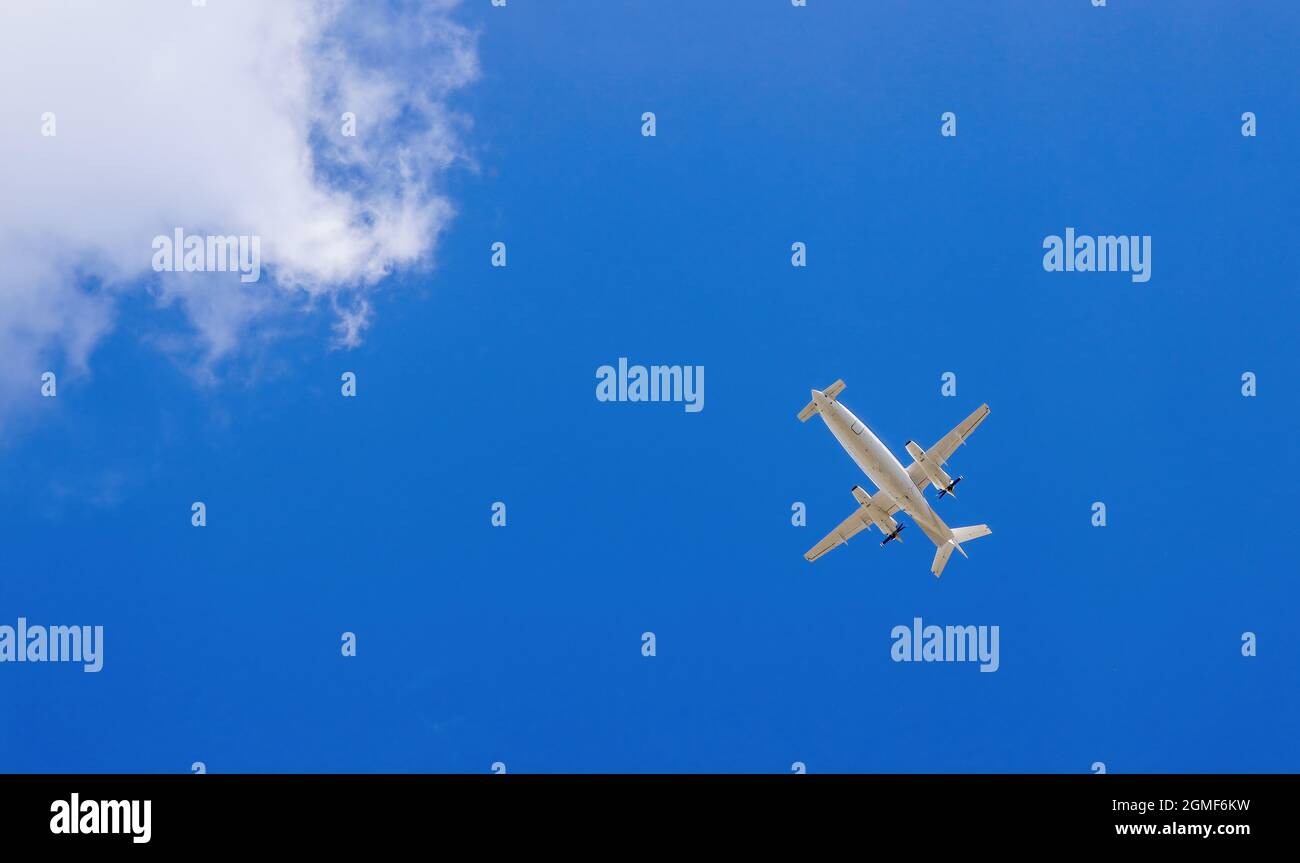 Small twin-engine turboprop business aircraft flying under blue sky viewed from below. Bottom view of airplane flying on bright sky background with cl Stock Photo