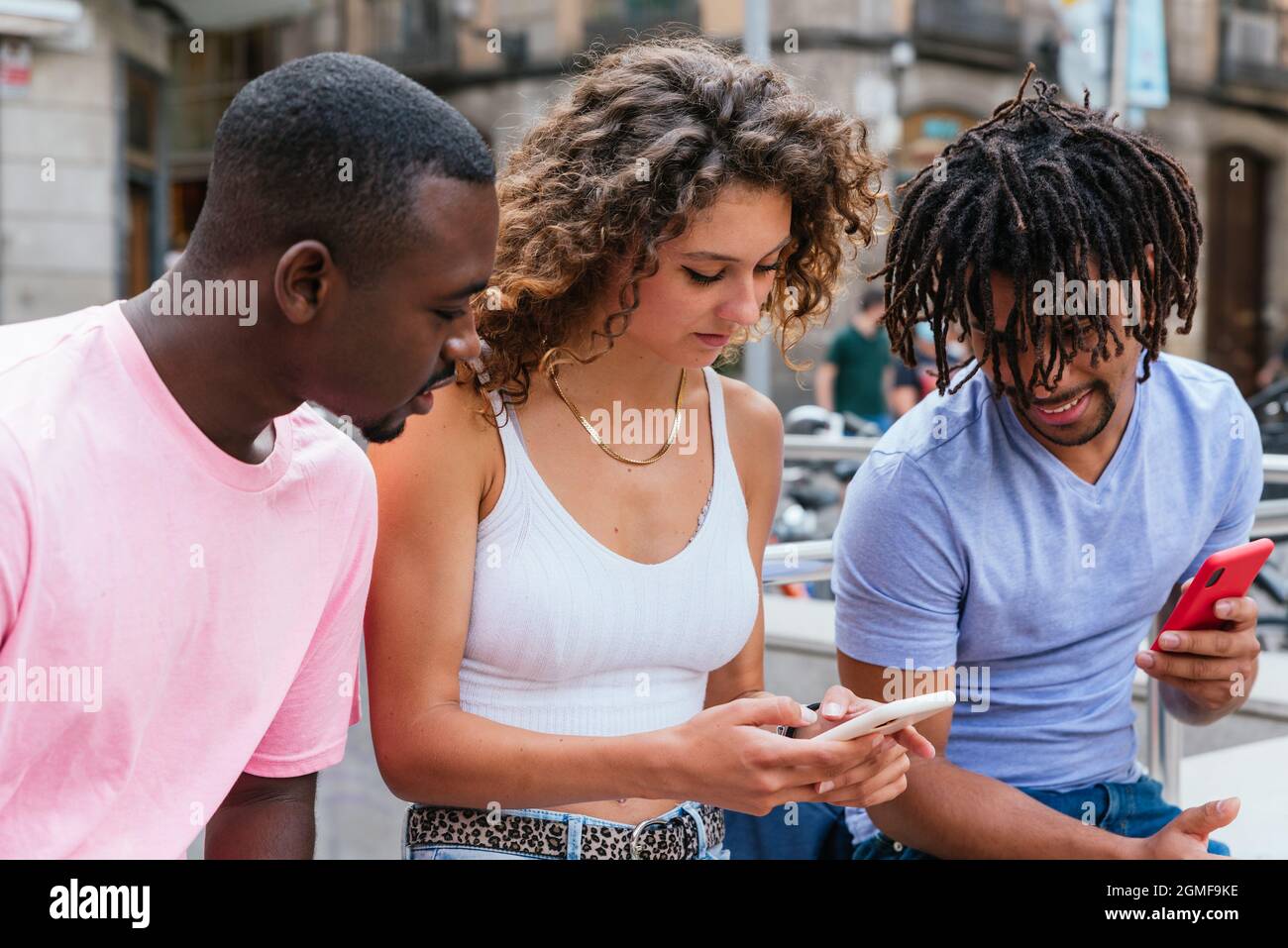 caucasian young woman showing her phone screen to african and latin male friends Stock Photo