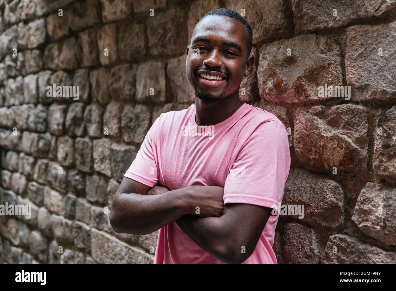 horizontal portrait of an afro american young man. He is looking at camera with a stone wall on the background Stock Photo