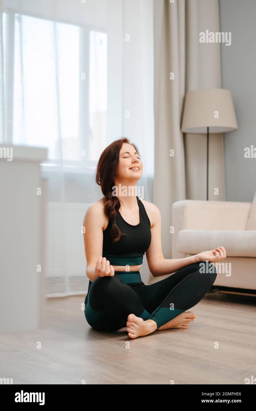 Young happy athlete in the lotus position is sitting on the floor of ...