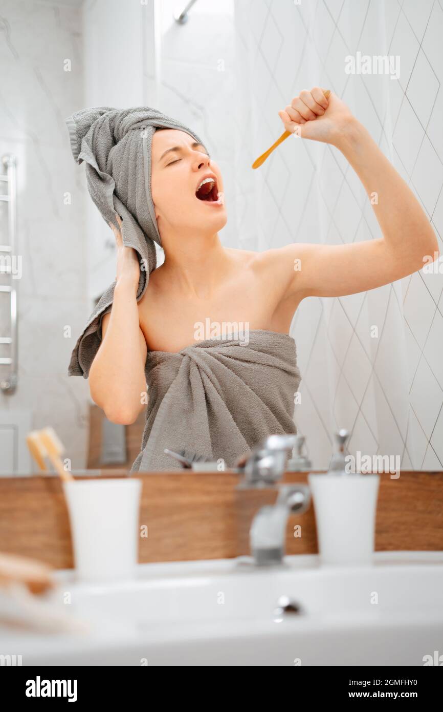 Women after a shower brushes her teeth and sings into a wooden toothbrush. Stock Photo