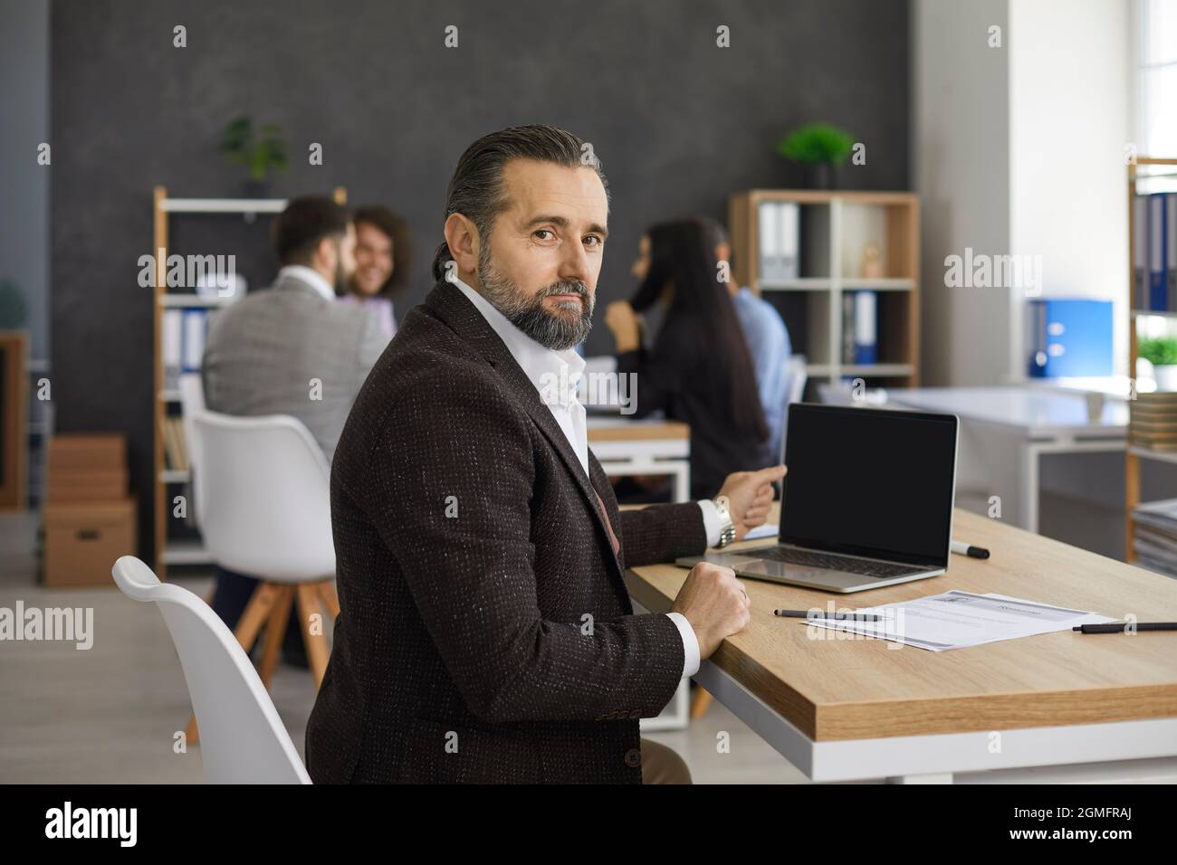 Portrait of senior business executive sitting at desk with laptop in modern office Stock Photo