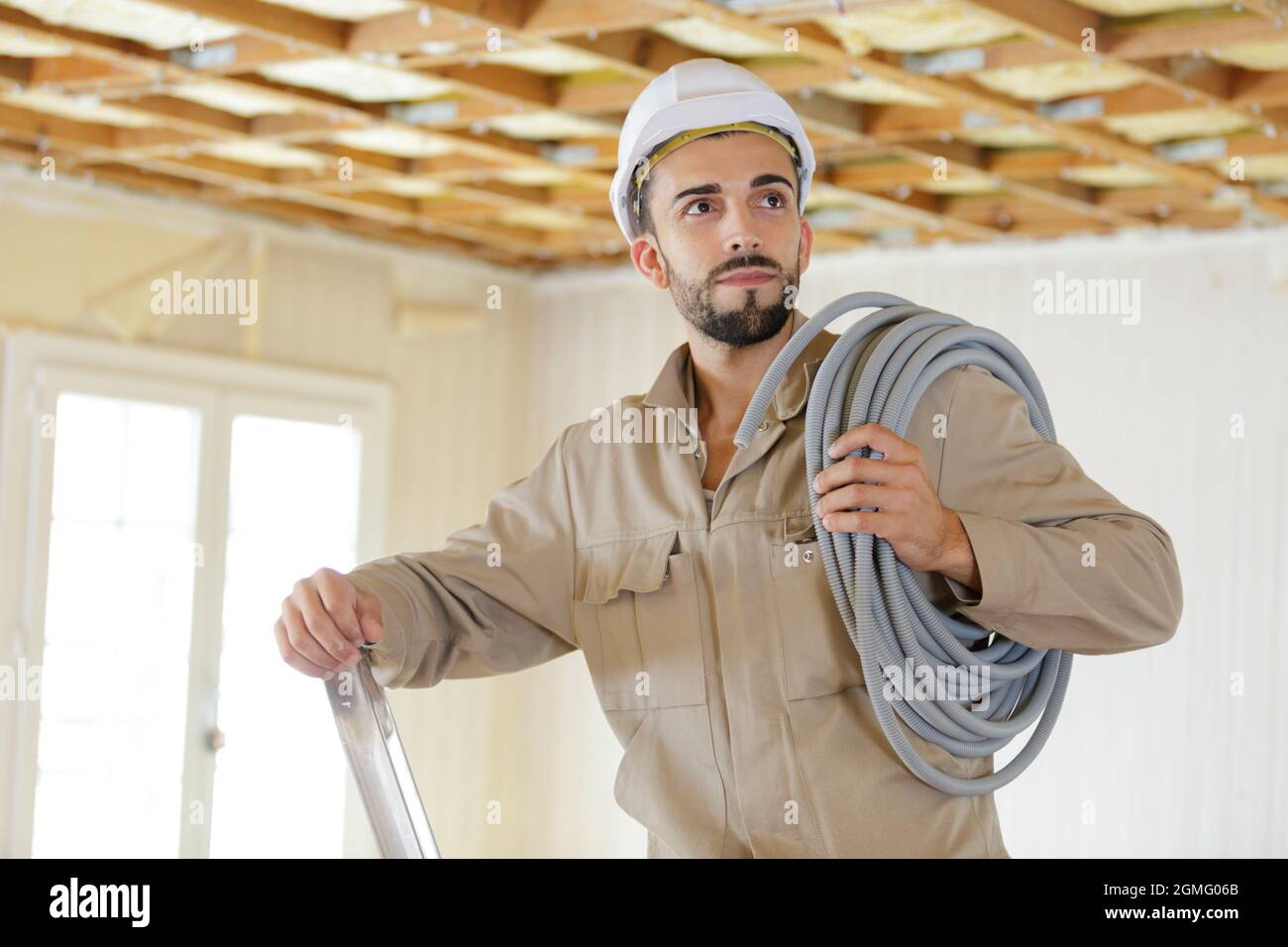 tradesman on stepladder with reel of cable on his shoulder Stock Photo