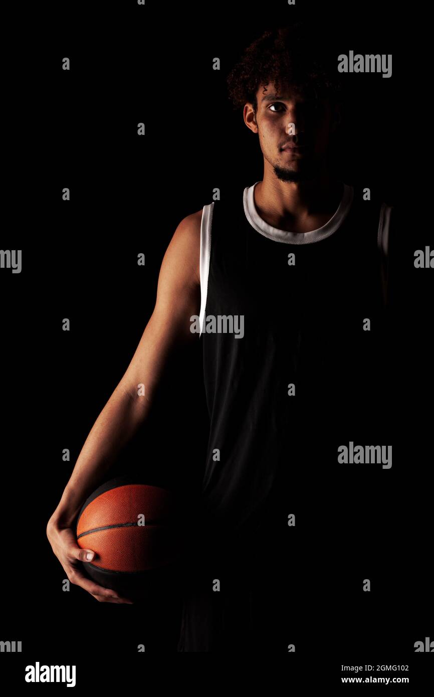 Professional basketball player holding a ball against black background. Serious concentrated african american man in sports uniform. Stock Photo