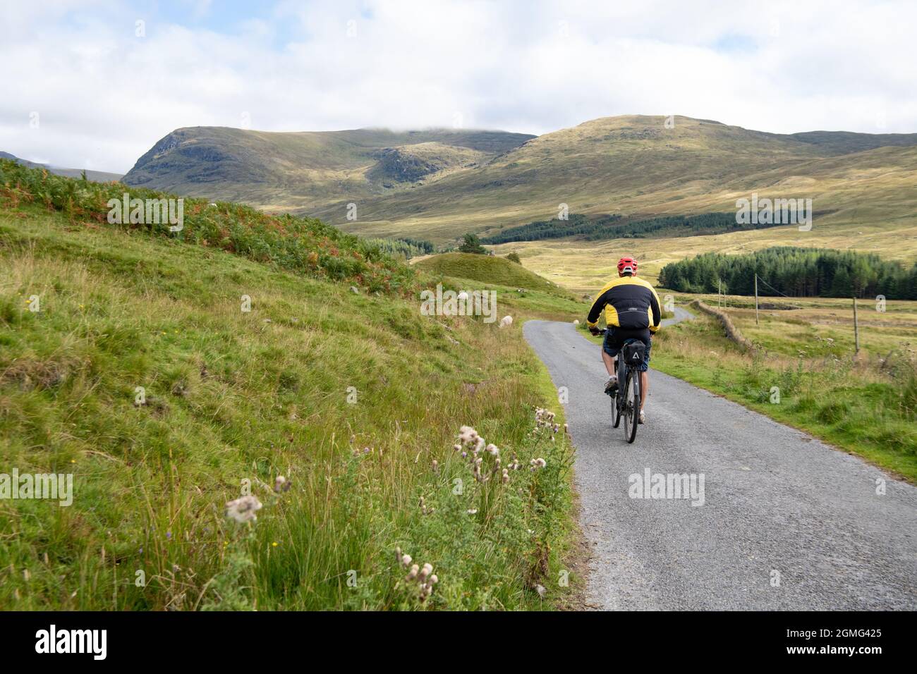 Man cycling on electric bike e-bike in Glen Lyon on the west side of Bridge of Balgie, cycling towards hill with Robert Campbell cairn, Scotland, UK Stock Photo