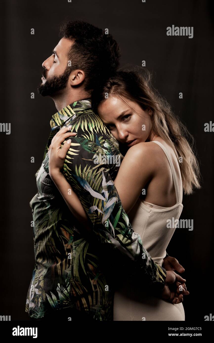 Couple posing on black background. Girl hugging boy from behind Stock