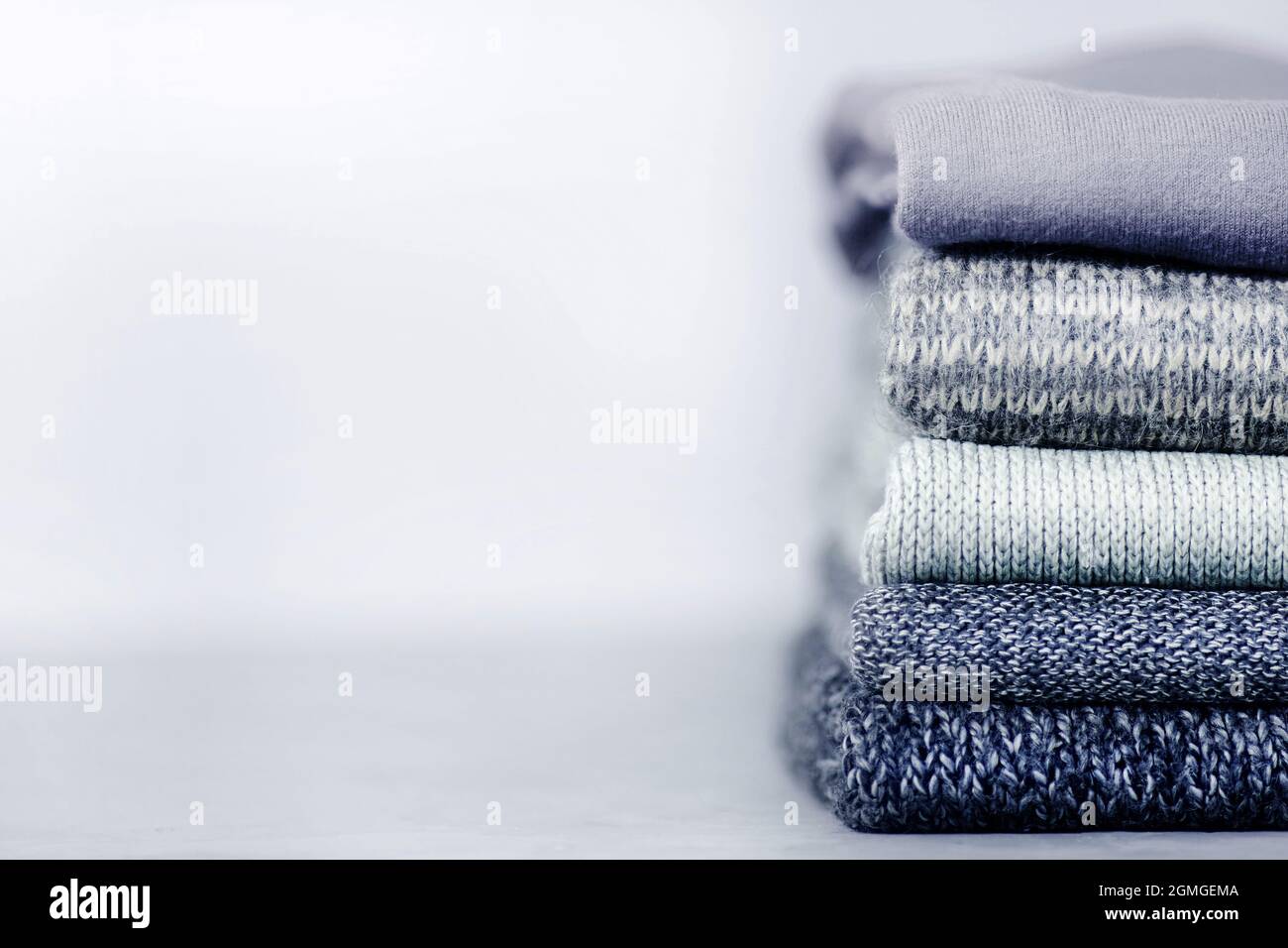 Stack of knitted jumpers and sweaters on a gray concrete blurry background. Copy space Stock Photo