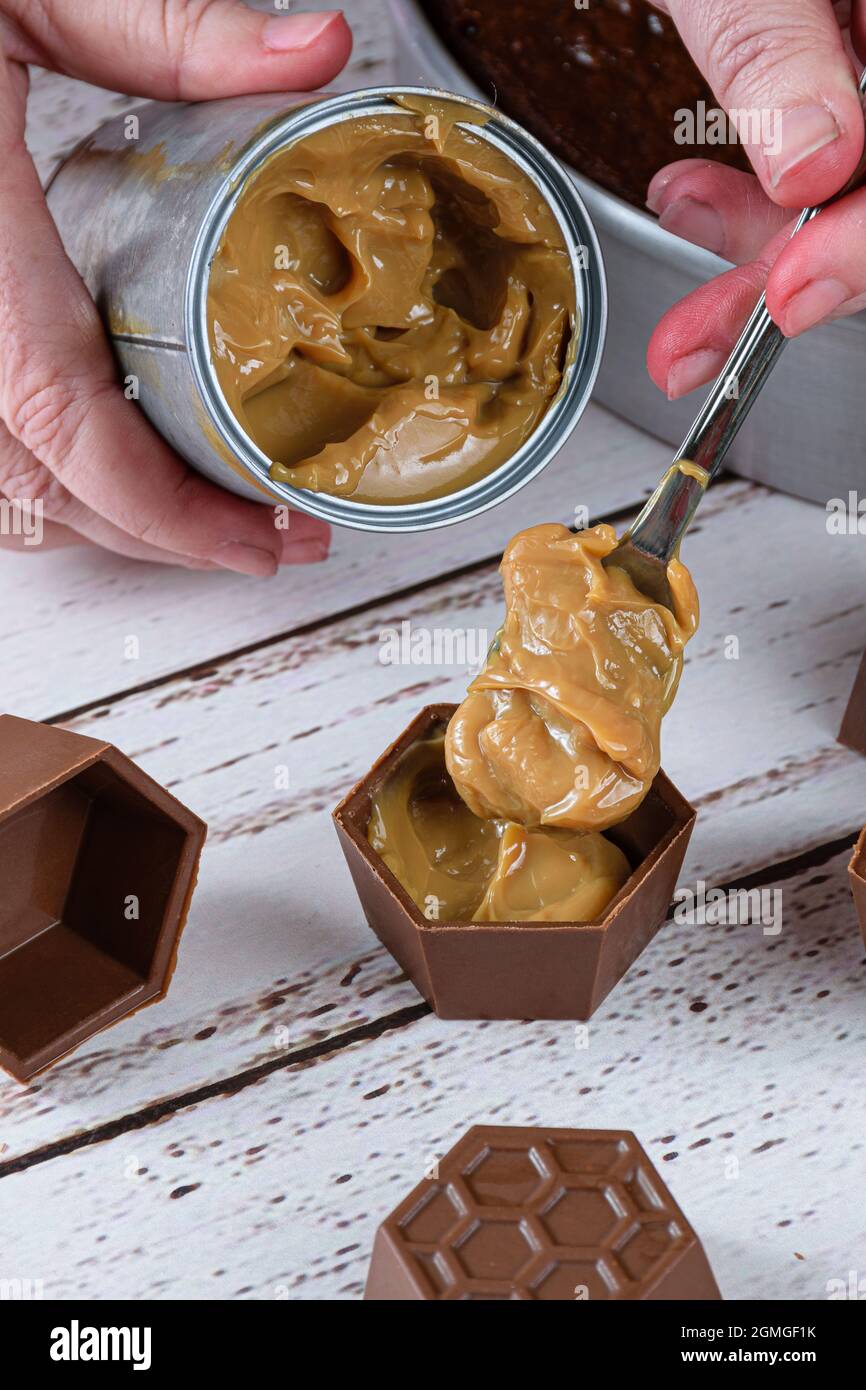 Confectioner putting a spoon of dulce de leche in small chocolate molds to make Brazilian honey cake. Stock Photo