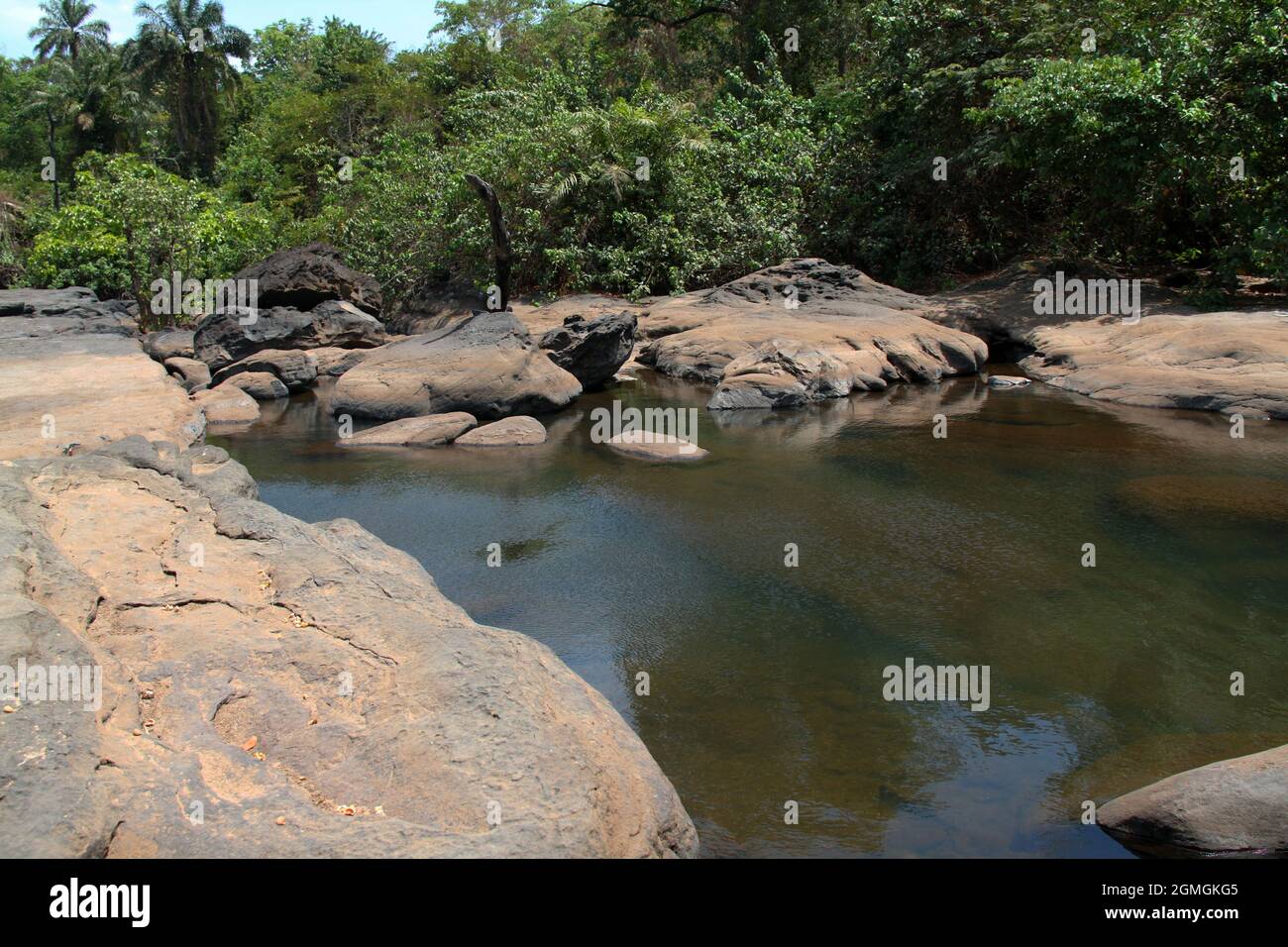 A pond of stream fed clear, warm  water, surrounded by large rocks and trees in inland Guinea, West Africa, on a sunny day. Stock Photo