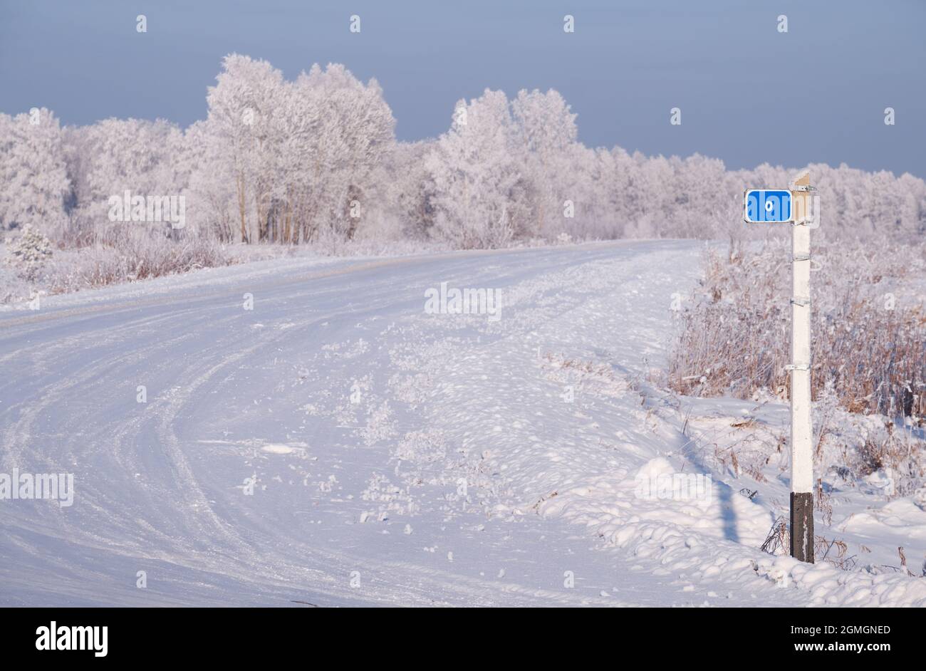 Winter road under snow. The beginning of the road with a zero kilometer sign. Siberian natural winter season landscape. Frozen birch trees covered wit Stock Photo