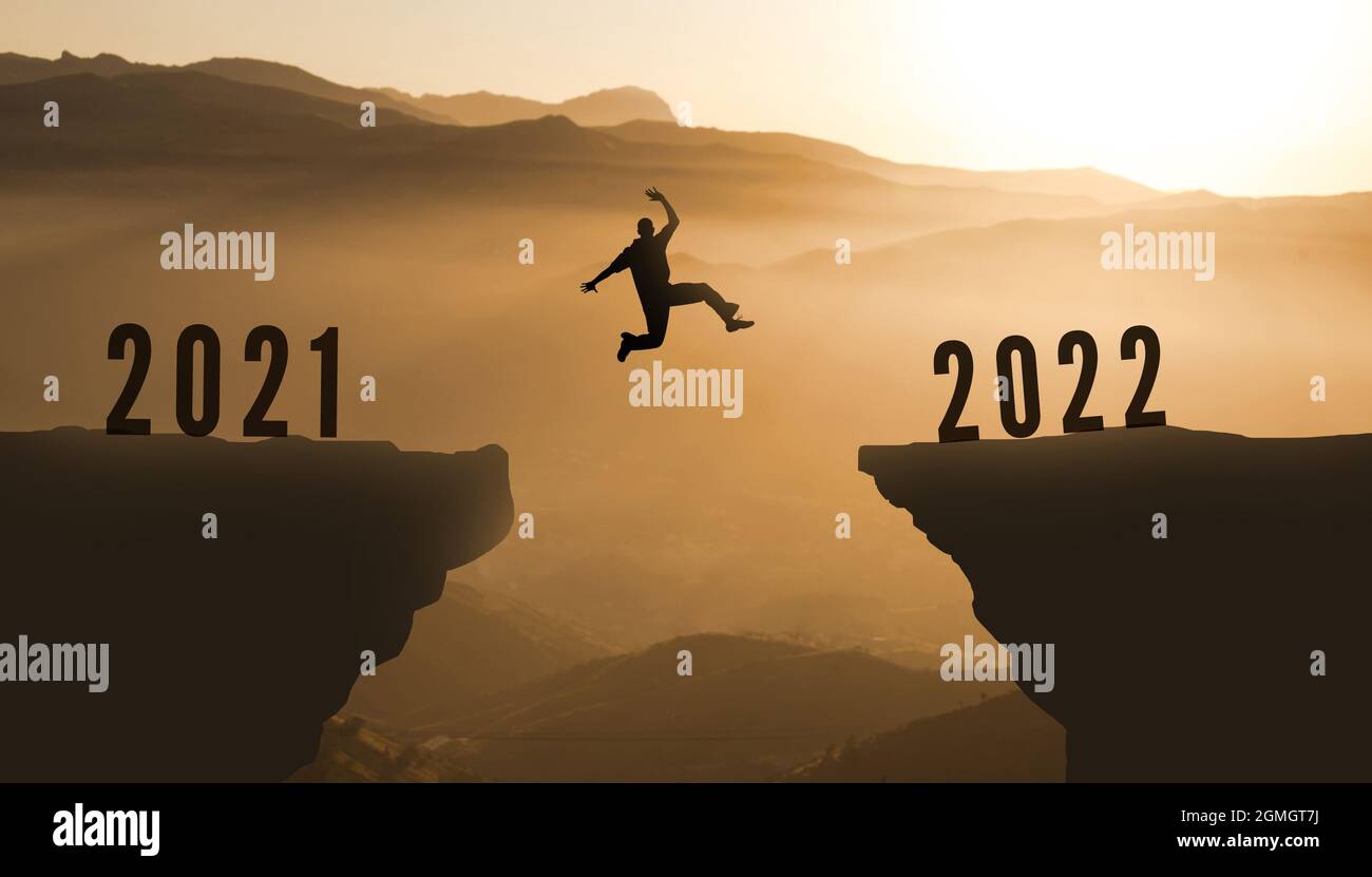 Man Silhouette Jumping from 2021 to 2022 Over Mountain. happy new year  2022. Sunset Mountains background. Young guy Jumps between two Cliffs or  two ye Stock Photo - Alamy