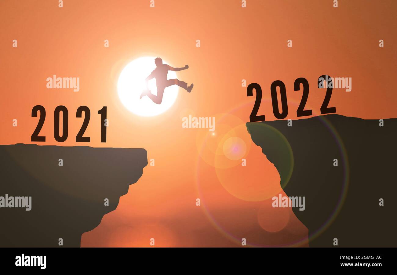 Man Jumping from 2021 to 2022 Over Cliff . happy new year 2022. Sunset background Young guy Jumps between two Cliffs or two years concept Stock Photo